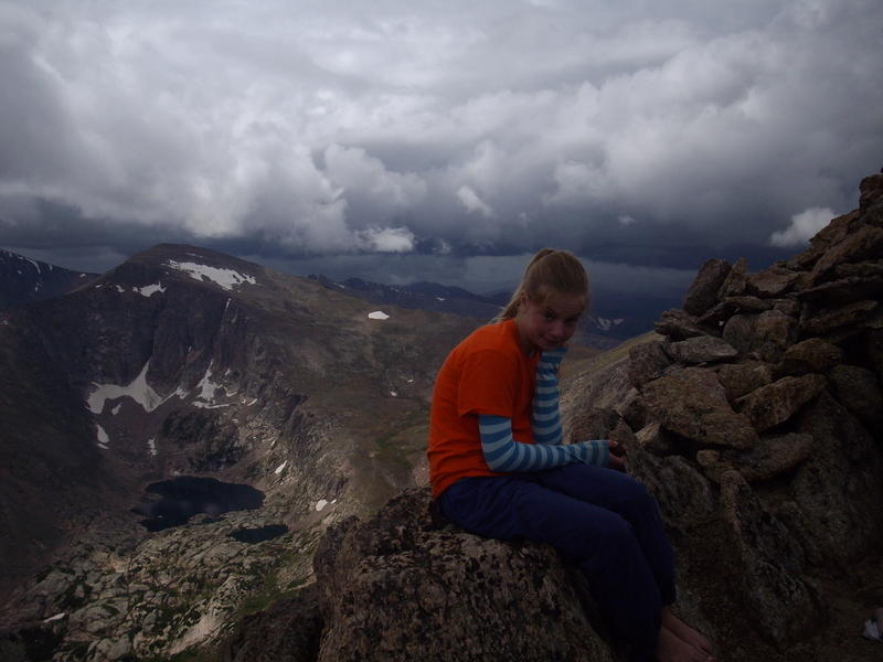 Elizabeth taking a break on the summit of Mummy with nasty storm clouds brewing behind.